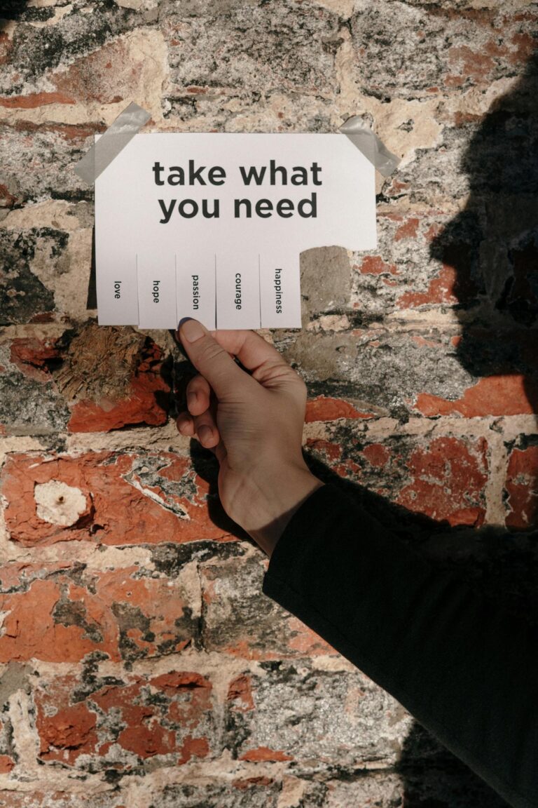 A hand holding a paper note with motivational text against a rustic brick wall.